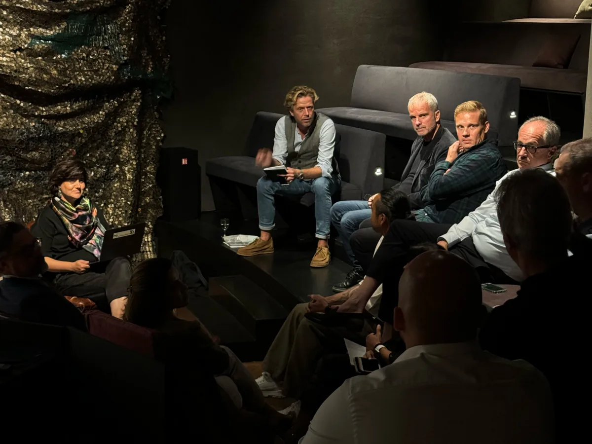 Gruppe von Teilnehmer:innen bei einer moderierten Diskussionsrunde in einem dunklen Veranstaltungsraum