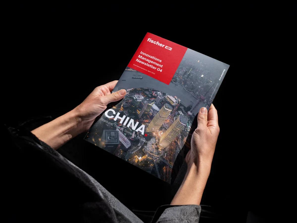 Zwei Haende halten eine gedruckte Ausgabe des fischer Innovations Management Newsletters mit China-Titelstory und Skyline von Shanghai auf dem Cover.