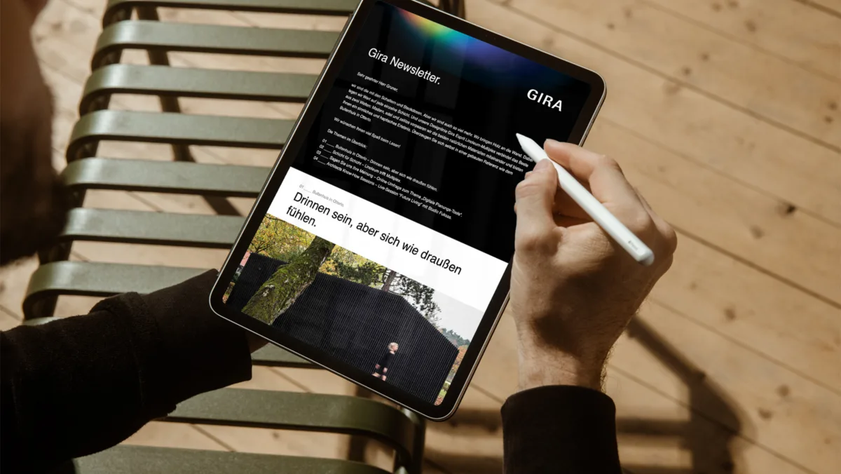 Person hält ein iPad mit Apple Pencil und liest den Gira Newsletter mit einem Architektur-Beitrag.