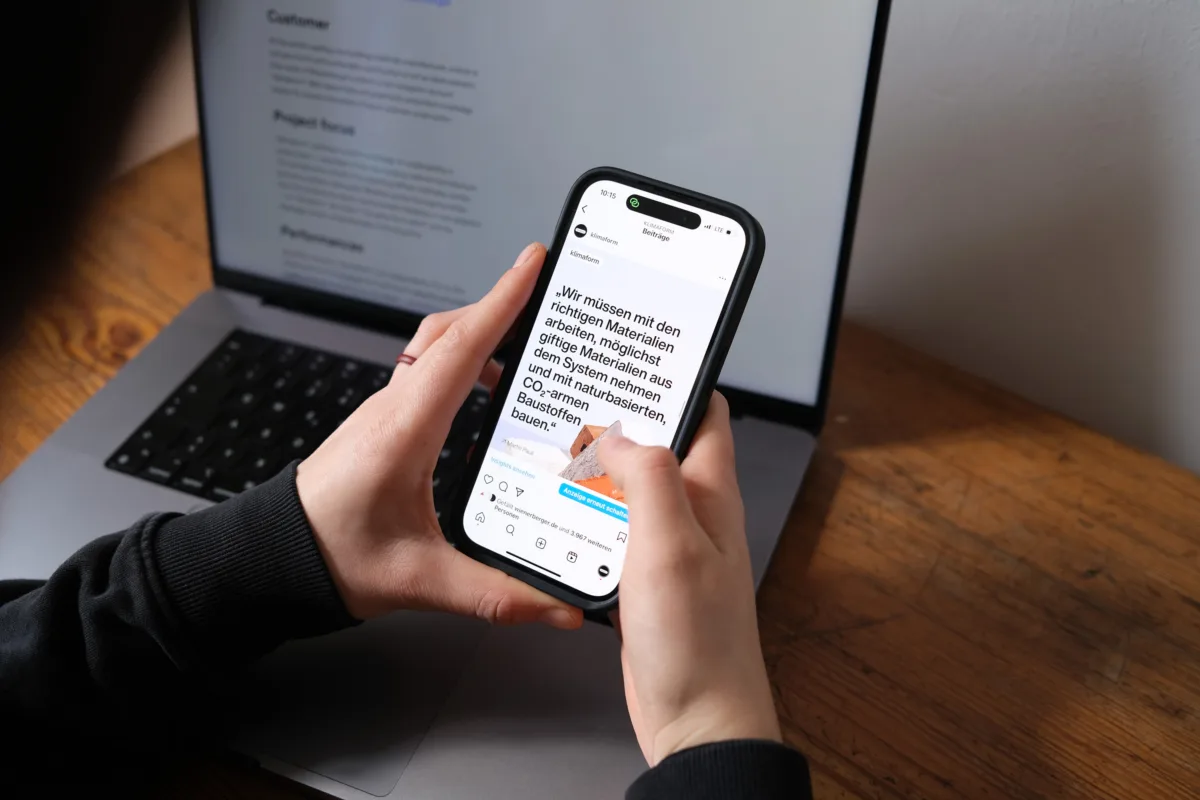 Hände halten ein Smartphone mit einem Instagram-Post des Klimaform-Kanals vor einem aufgeklappten Laptop