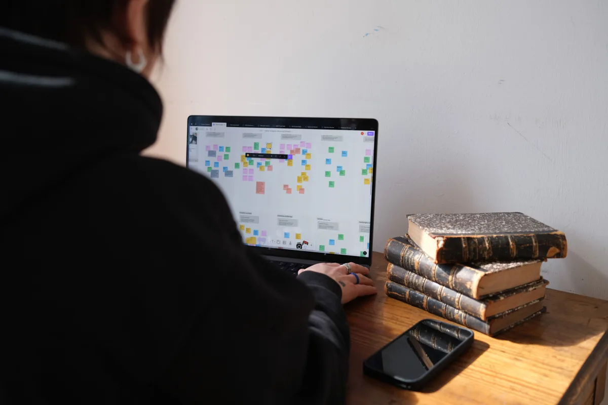 Person arbeitet an einem Laptop mit farbigem Redaktionsplan, daneben ein Bücherstapel und Smartphone
