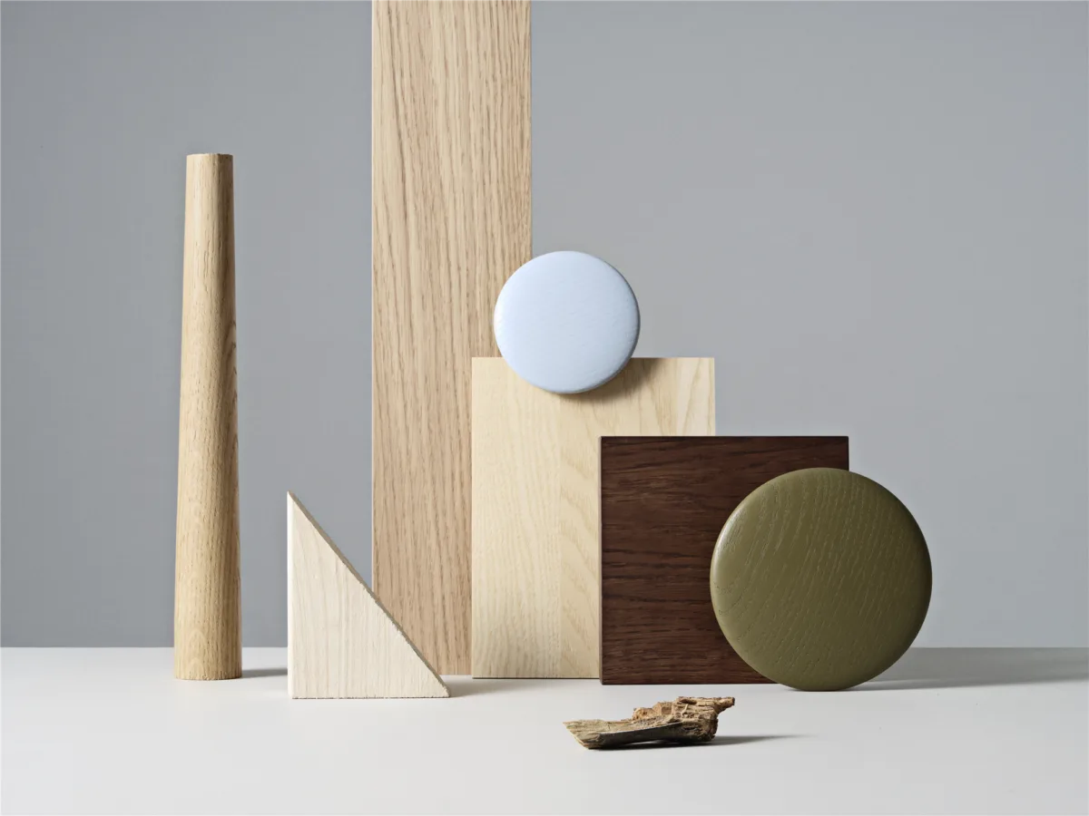 Stillleben mit Holzmustern, Farbflächen und geometrischen Formen in der Muuto-Farbwelt. Helle Hölzer, Olivgrün und Hellblau vor grauem Hintergrund.