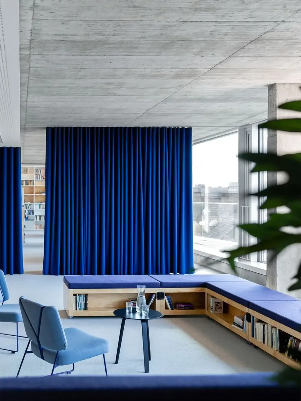 Ein in blauen Tönen gehaltenes Wohnzimmer, mit passenden blauen Vorhängen, gestaltet im Stil des Beton-Brutalismus, der eine kräftige und rohe Ästhetik ausstrahlt.