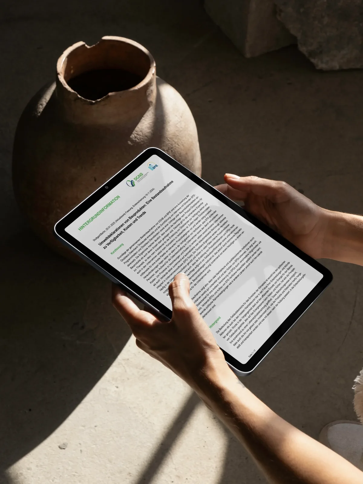 Hände halten ein Tablet mit einem digitalen Dokument über Umweltproduktdeklarationen (EPDs) vor dem Hintergrund einer keramischen Vase.