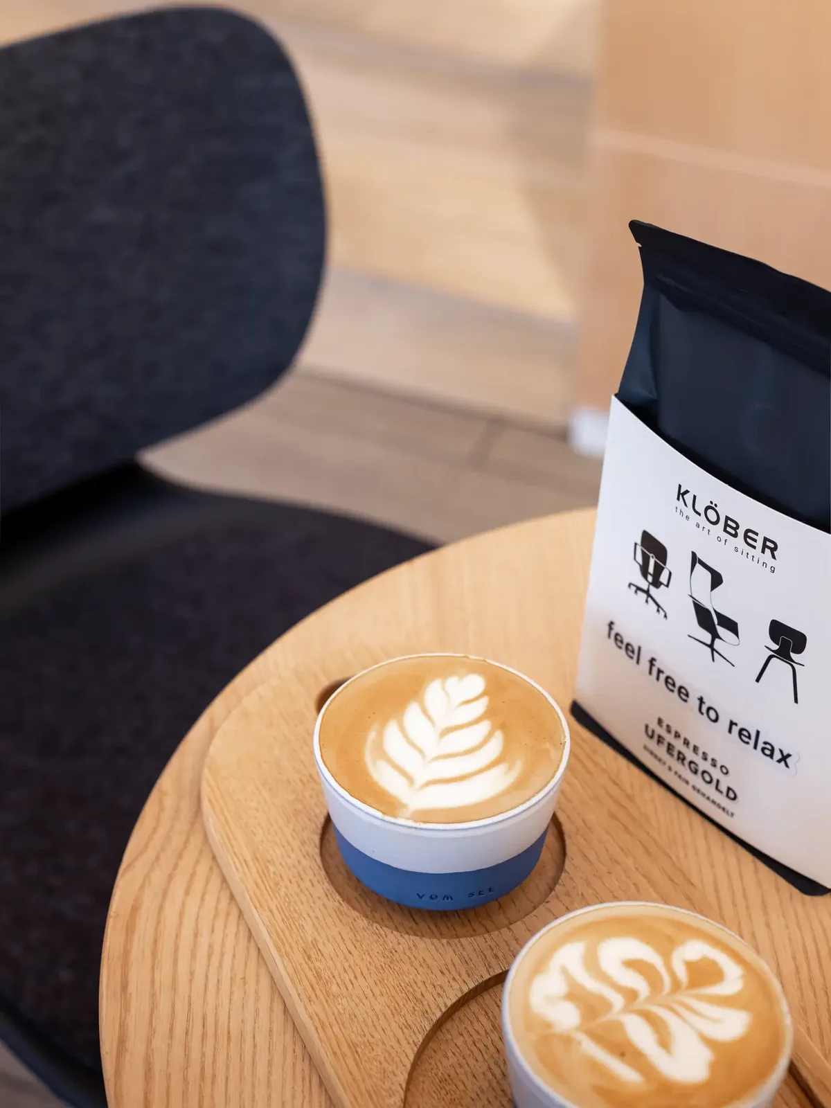 Zwei Cappuccinos mit Latte Art auf Holztisch neben einer Espressopackung von Klöber.