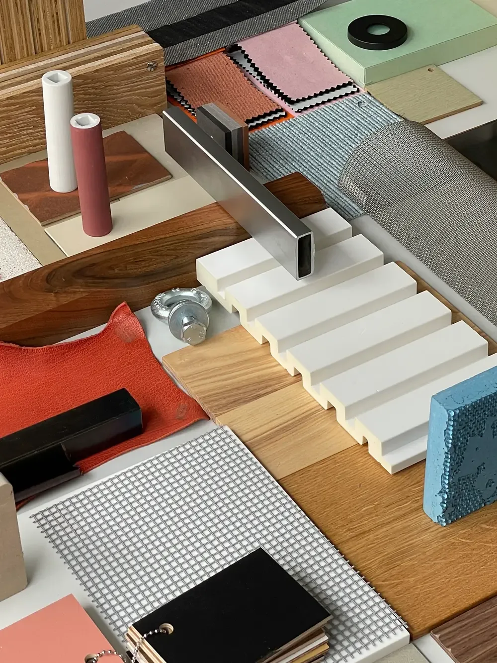 Materialcollage mit verschiedenen Bau- und Designproben, darunter Holz- und Metallstücke, Netze, Textilien und farbige Platten.