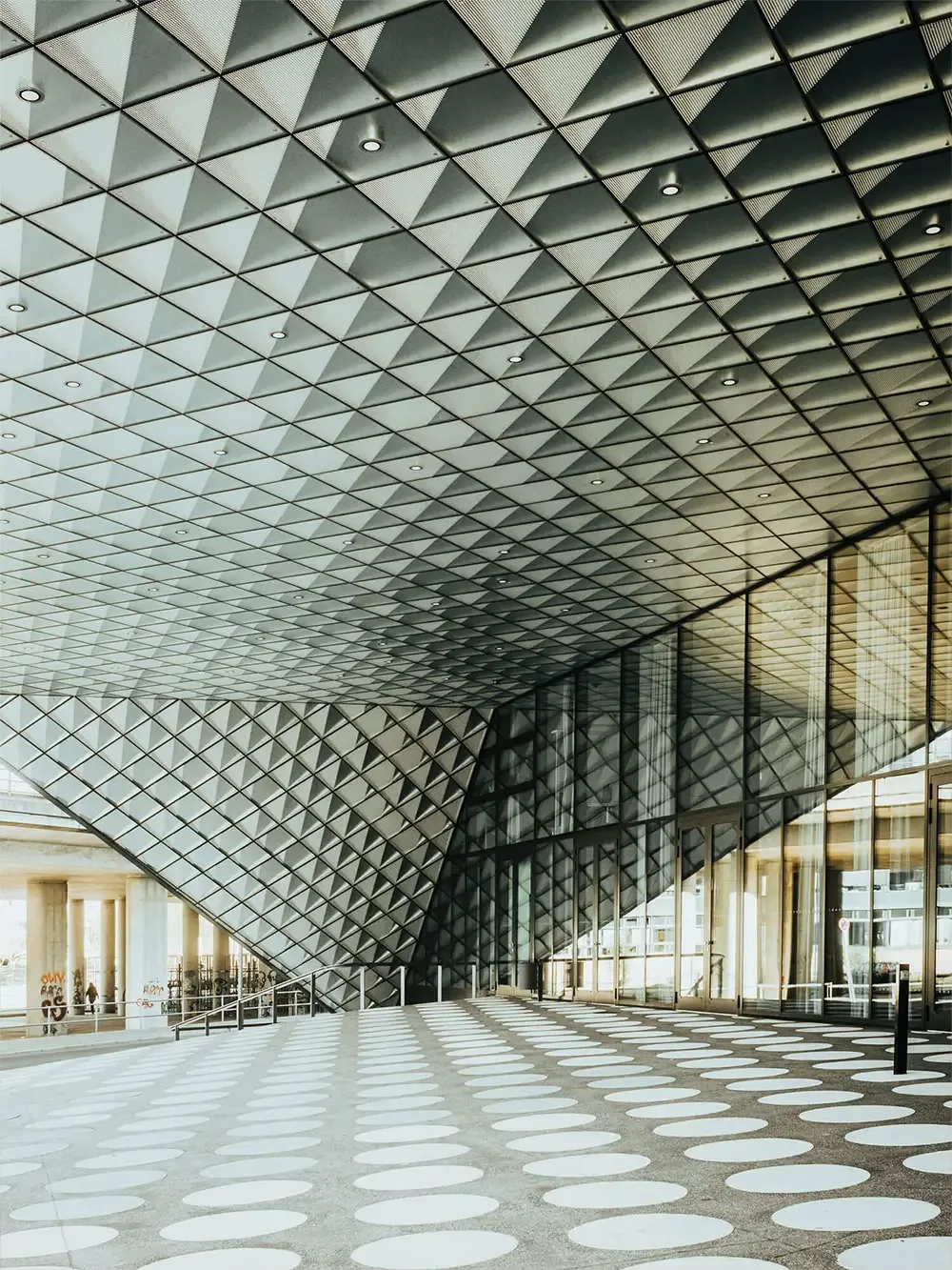 Ein modernes Gebäude mit Glas und weißen Fliesen. Kunstvolle Deckengestaltung mit scharfen, kantigen Linien.