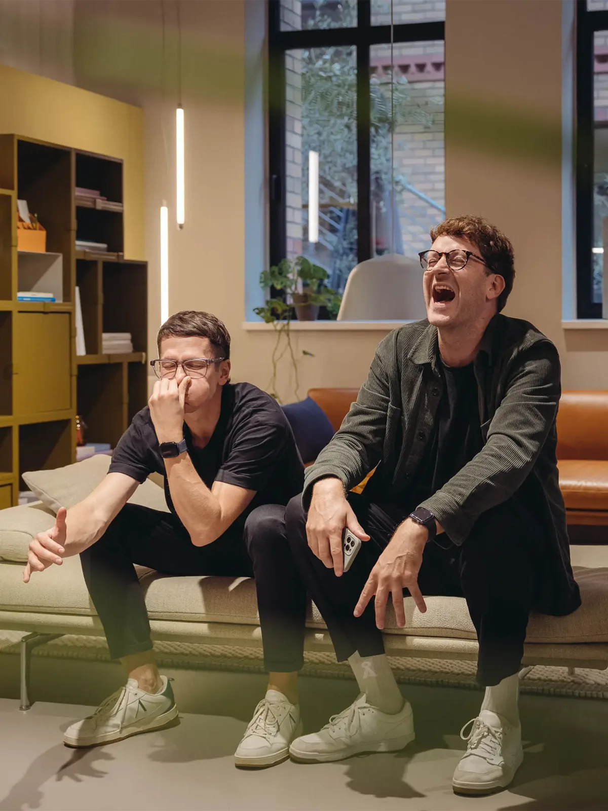 Die hej.build Gründer Michael Rahmfeld und Hannes Eberlein sitzen lachend auf einer Couch im Büro.
