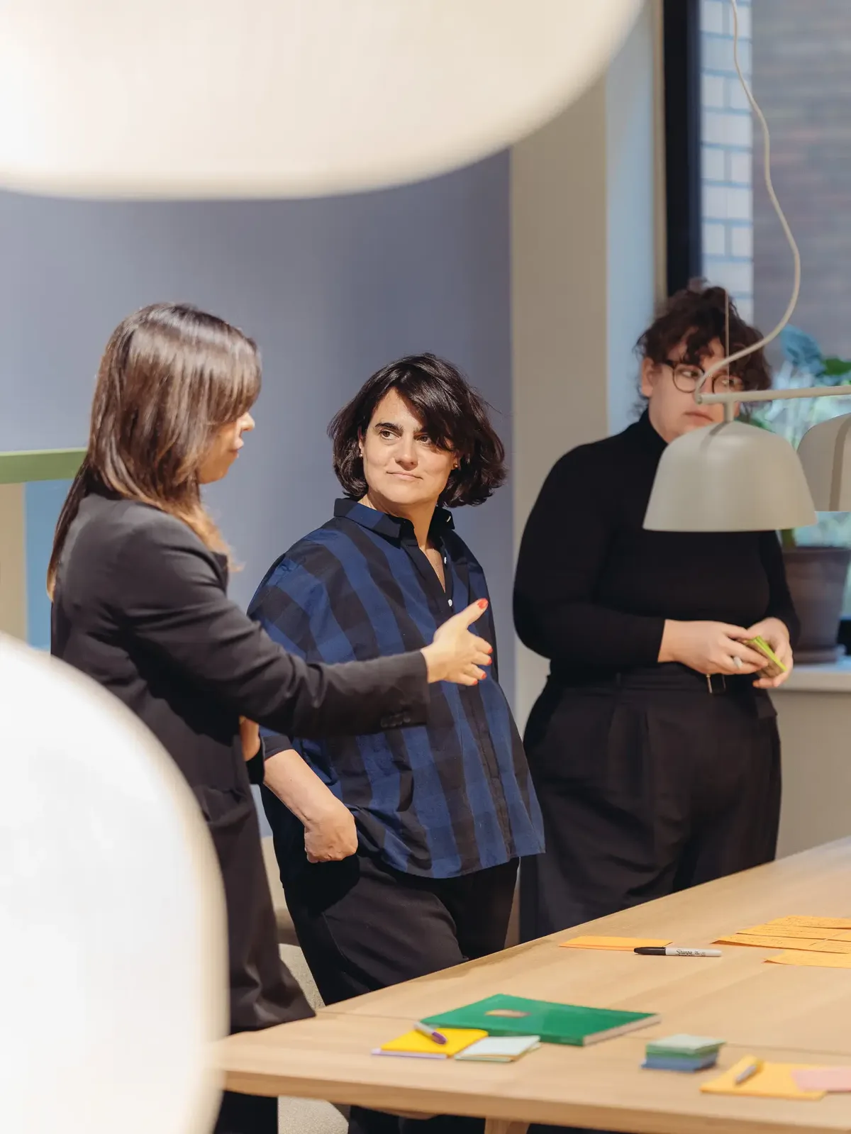 Drei Architektinnen und Designerinnen in einer kreativen Workshop-Situation, diskutieren Konzepte am Tisch.