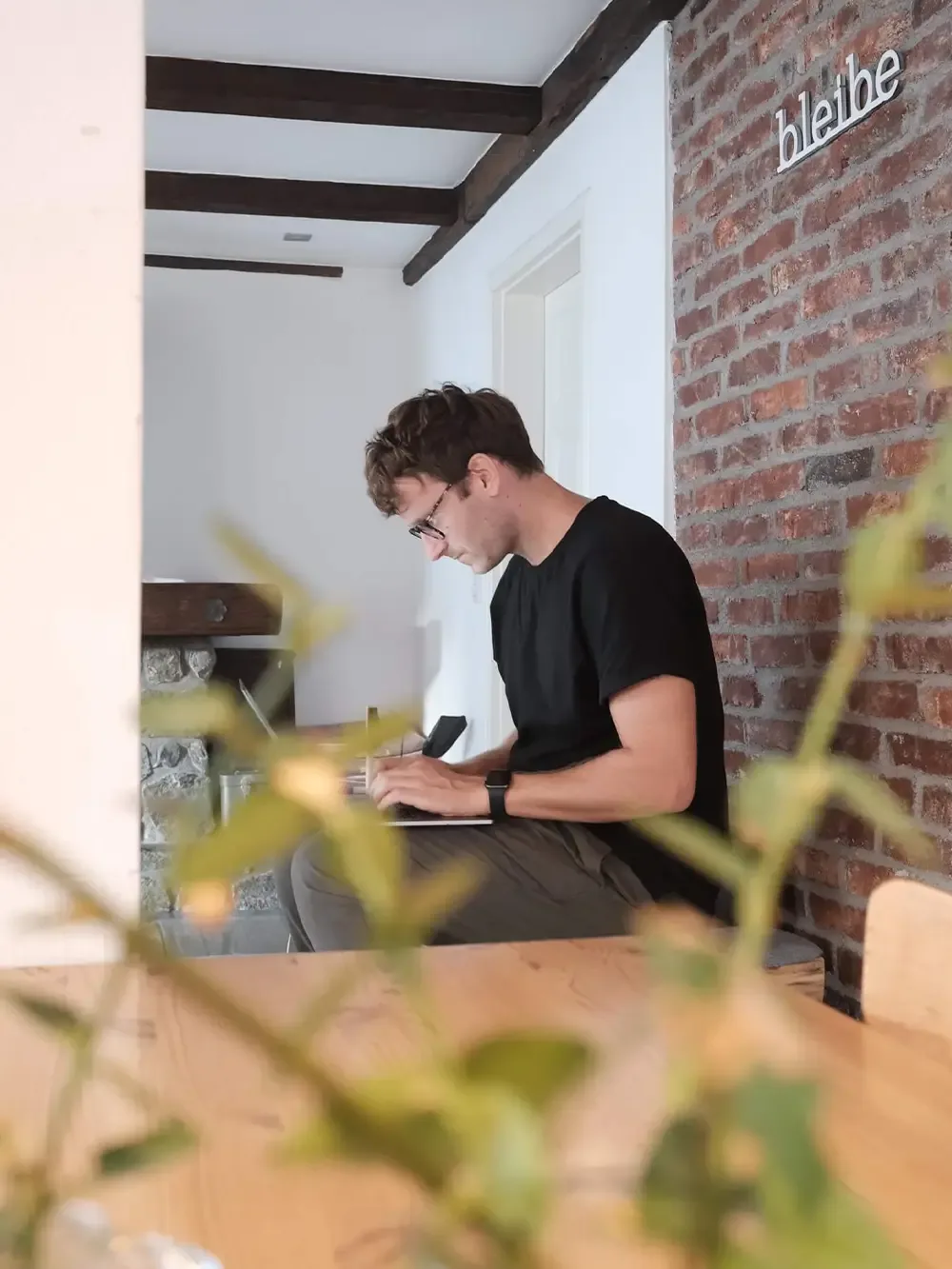 Hannes Eberlein, Gründer und Geschäftsführer von hej.build, arbeitet konzentriert an einem Tisch in einem Büro, umgeben von zwei Topfpflanzen.